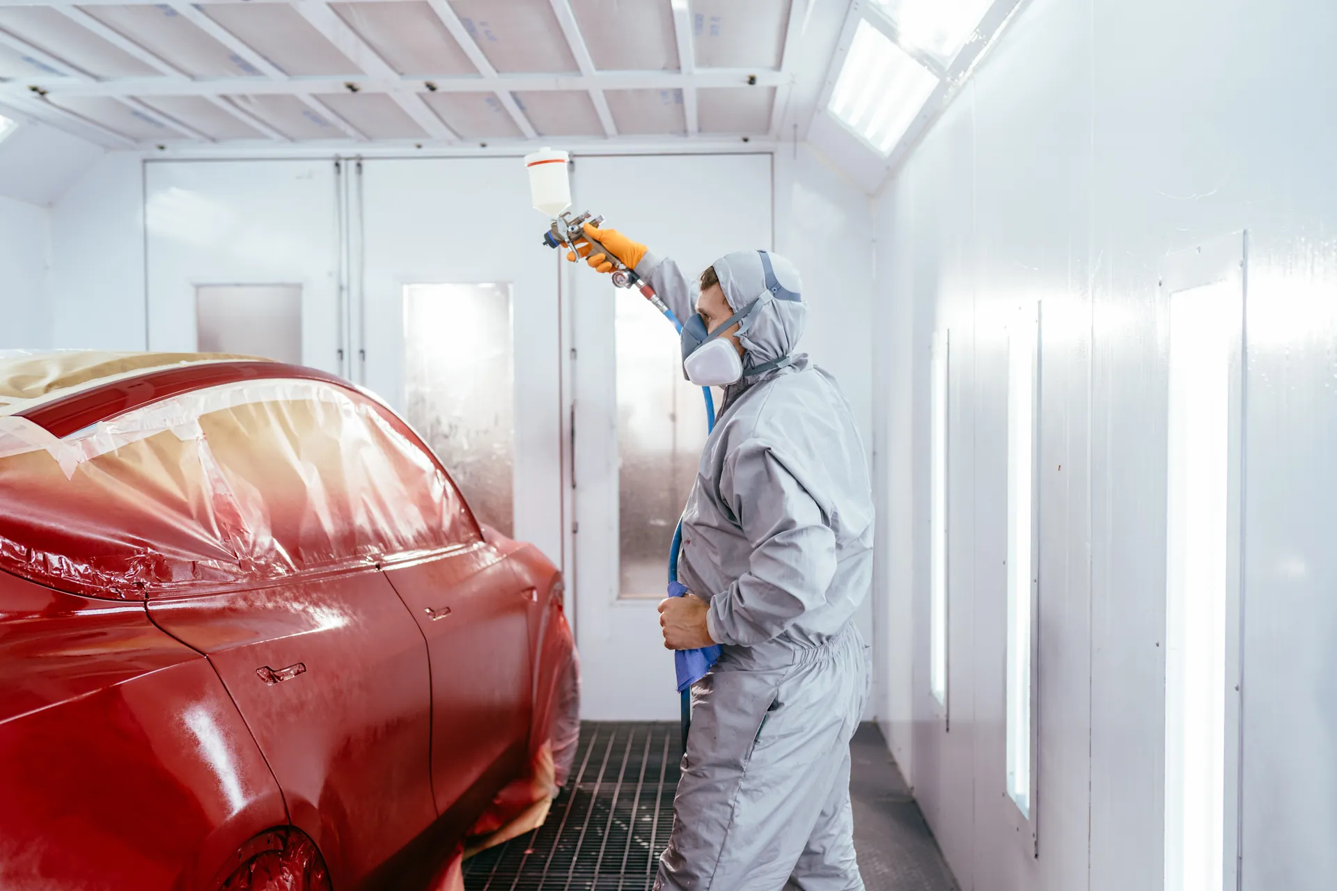 Peintre carrossier en combinaison appliquant la peinture en cabine