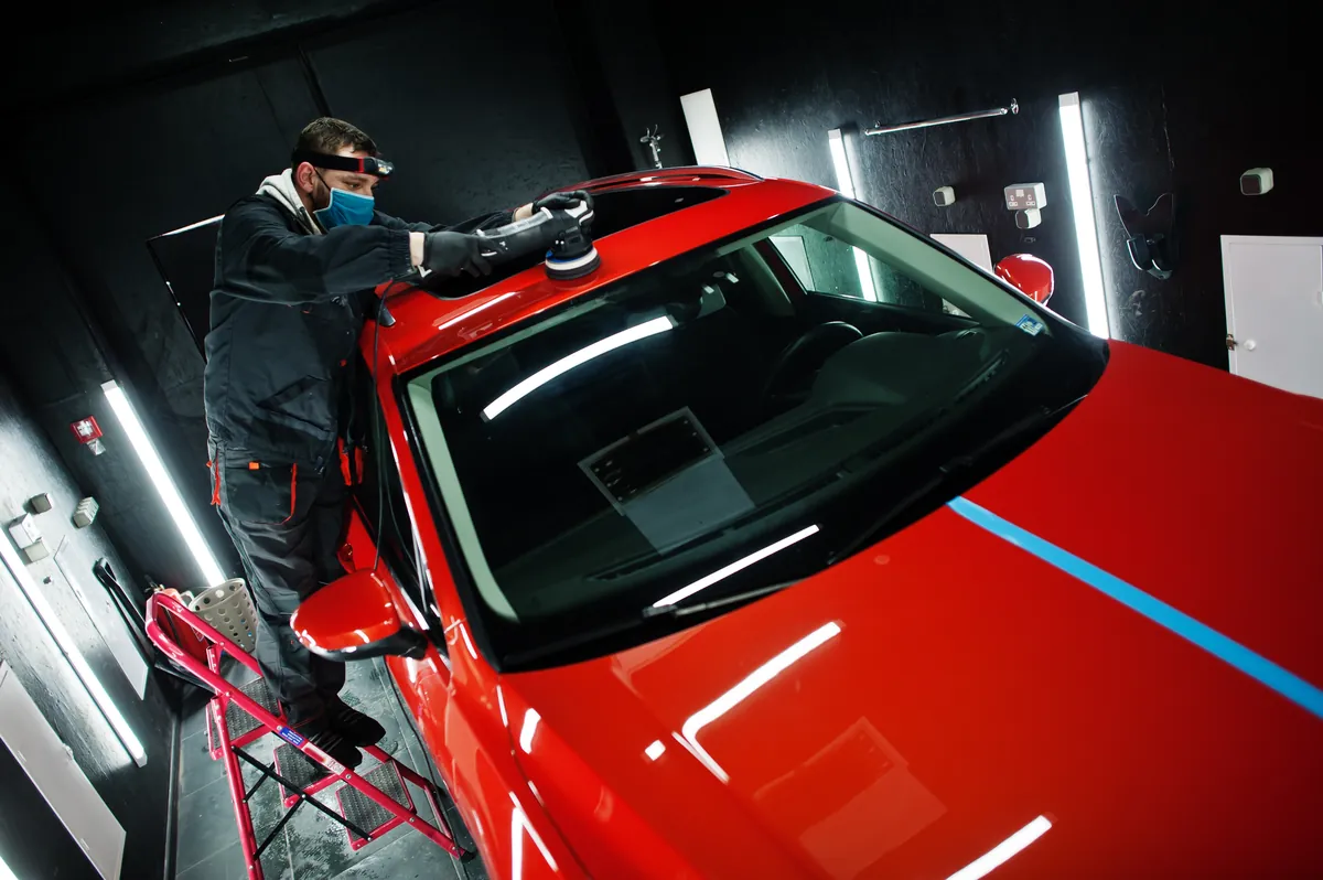 Carrossier polissant le capot d’une voiture rouge en cabine